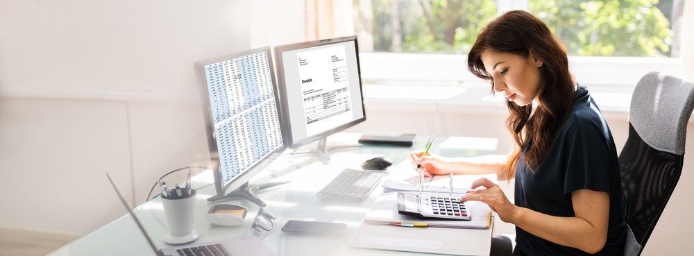 An accountant uses her calculator and computer in an office setting to maintain accurate financial statements, a preventative step to avoiding potential TSBPA licensing issues.